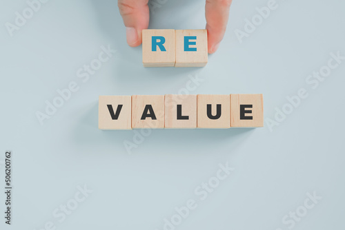 businessman's hand holding wooden cube blocks with Revalue text on blue pastel background