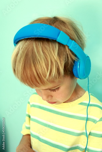 Adorable concentrated small 5s kid boy wearing blue headphones, looking down at tablet. Little boy with headphones playing the game device.