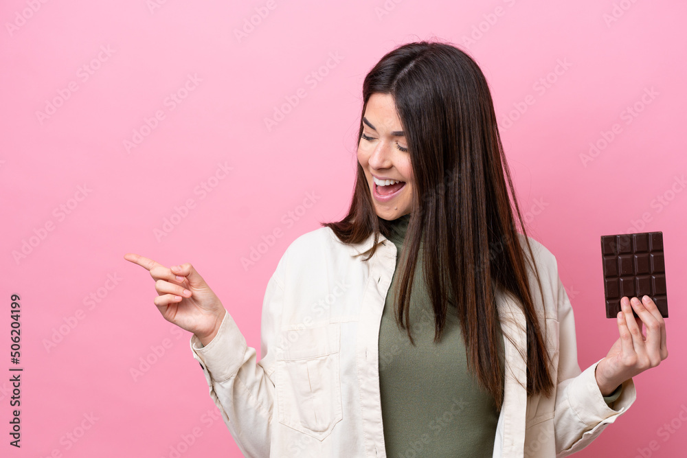 Young Brazilian woman with chocolat isolated on pink background pointing finger to the side and presenting a product Young Brazilian woman with chocolat isolated on pink background pointing finger to the side and presenting a product