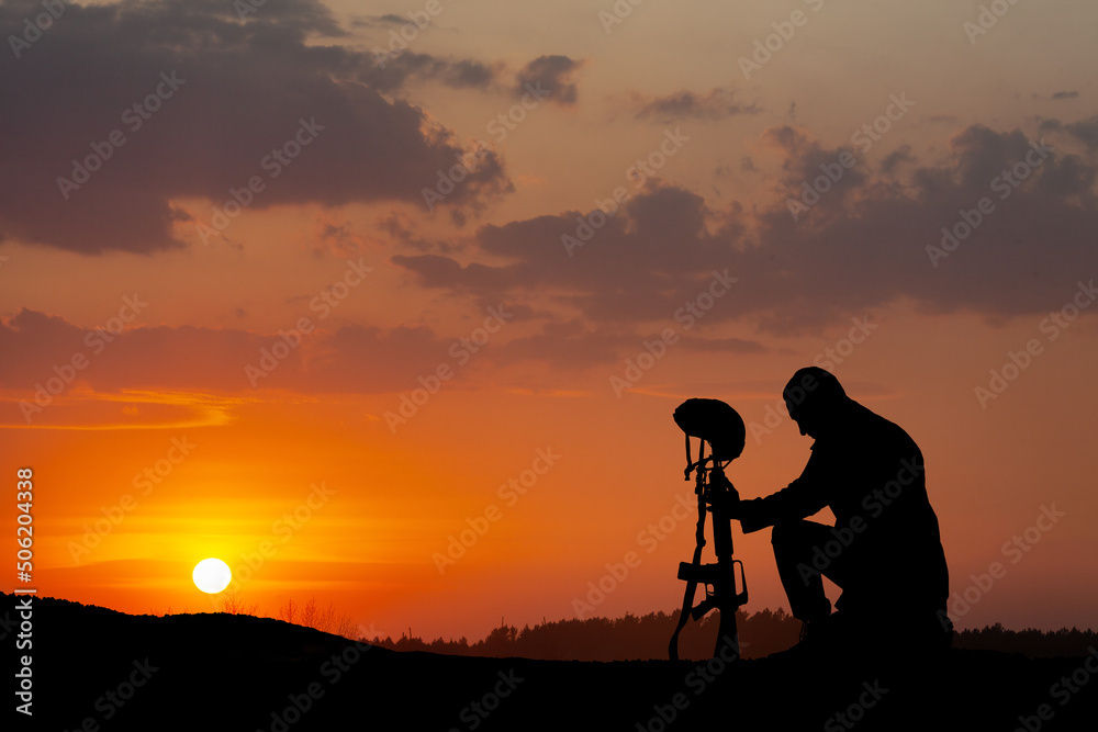Silhouette of soldier kneeling with his head bowed on a background of sunset or sunrise. Greeting card for Veterans Day, Memorial Day, Independence Day. Concept - patriotism, remember honor. Silhouette of soldier kneeling with his head bowed on a background of sunset or sunrise. Greeting card for Veterans Day, Memorial Day, Independence Day. Concept - patriotism, remember honor.
