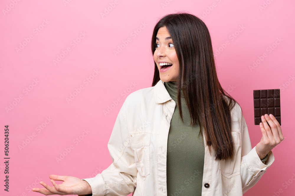 Young Brazilian woman with chocolat isolated on pink background with surprise expression while looking side Young Brazilian woman with chocolat isolated on pink background with surprise expression while looking side