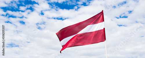Latvian flag waving in wind. Flag of Latvia on white cloudy sky background.