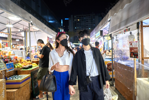 Lesbian couple in mask walking relaxed through an urban night fair
