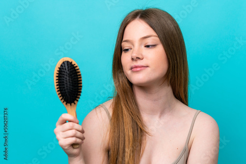 Young caucasian woman isolated on blue background with hair comb and looking it