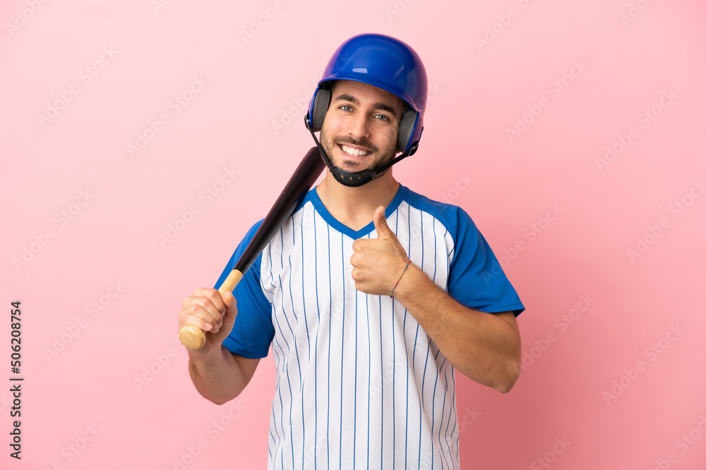 Baseball player with helmet and bat isolated on pink background giving a thumbs up gesture Baseball player with helmet and bat isolated on pink background giving a thumbs up gesture
