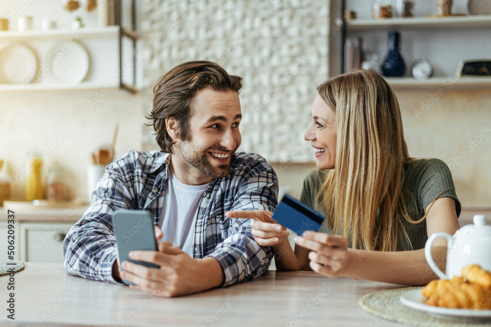 Glad surprised european millennial family with phone and credit card, blonde wife pointing finger at gadget Glad surprised european millennial family with phone and credit card, blonde wife pointing finger at gadget