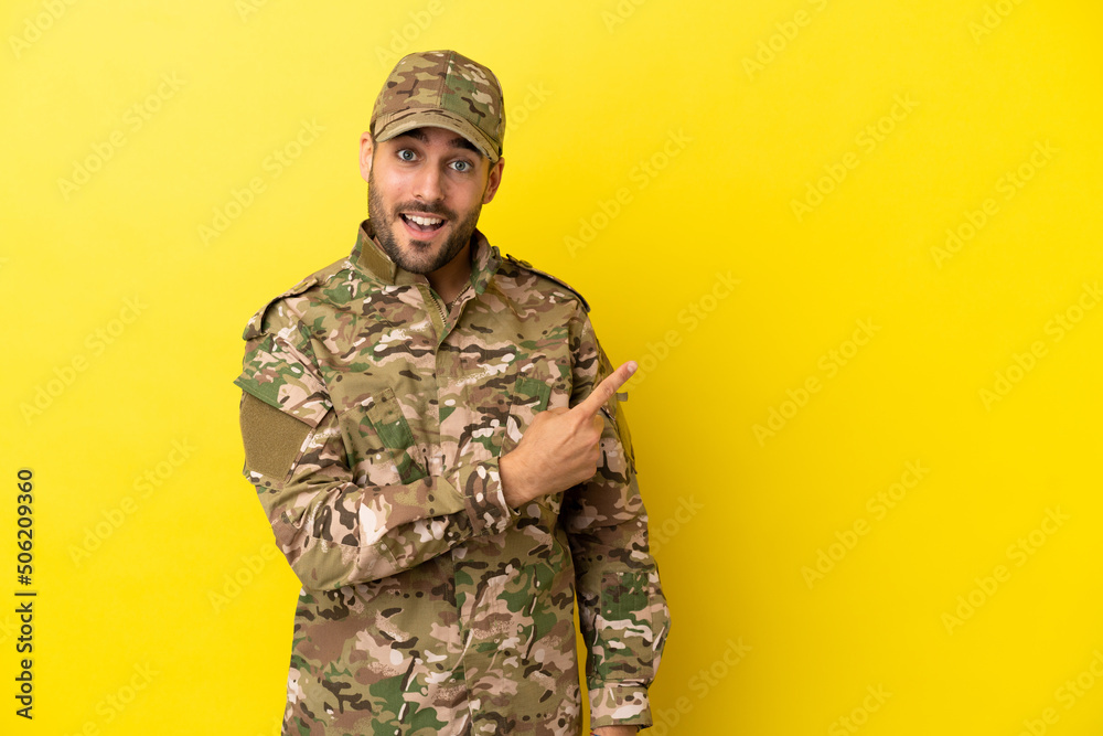 Military man isolated on yellow background pointing to the side to present a product Military man isolated on yellow background pointing to the side to present a product