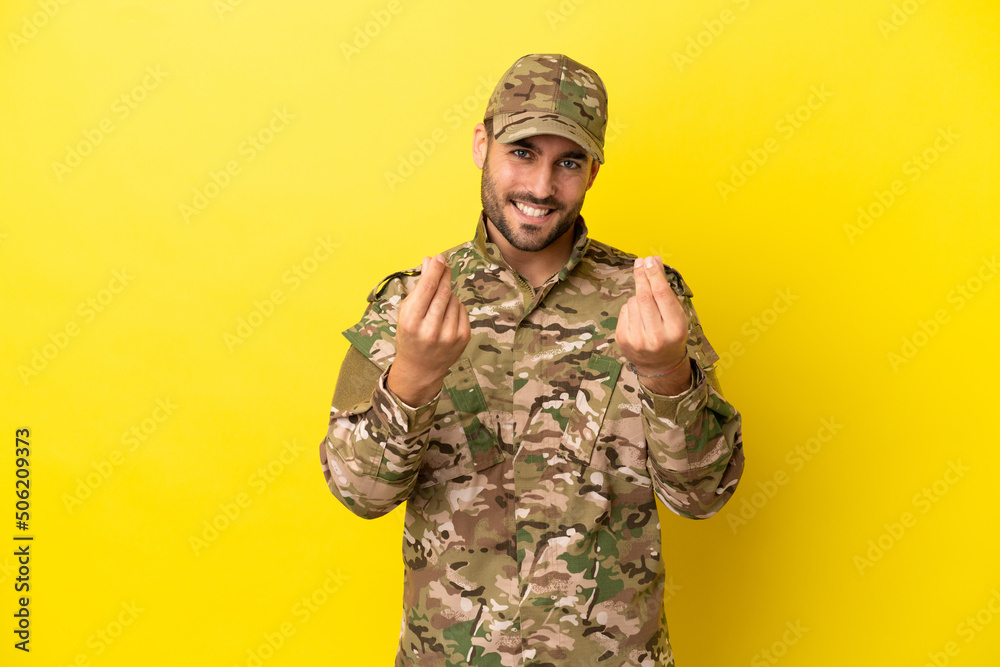 Military man isolated on yellow background making money gesture Military man isolated on yellow background making money gesture