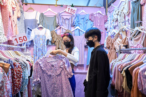 Asian non binary couple buying clothes in an urban night fair
