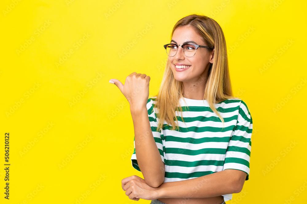 Blonde Uruguayan girl isolated on yellow background pointing to the side to present a product Blonde Uruguayan girl isolated on yellow background pointing to the side to present a product