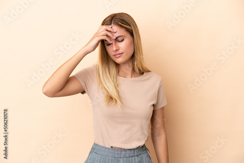 Blonde Uruguayan girl isolated on beige background with headache