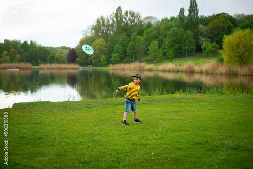 Little cute boy plays frisbee in the park against the background of green grass.