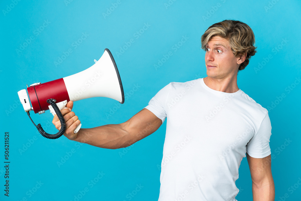 English man over isolated blue background holding a megaphone with stressed expression English man over isolated blue background holding a megaphone with stressed expression