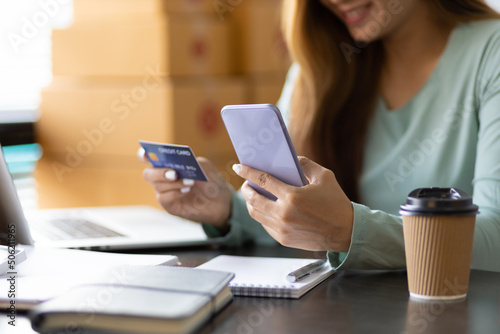 Woman holds a credit card and uses a mobile phone to check online balance and make online shopping. © Wasan