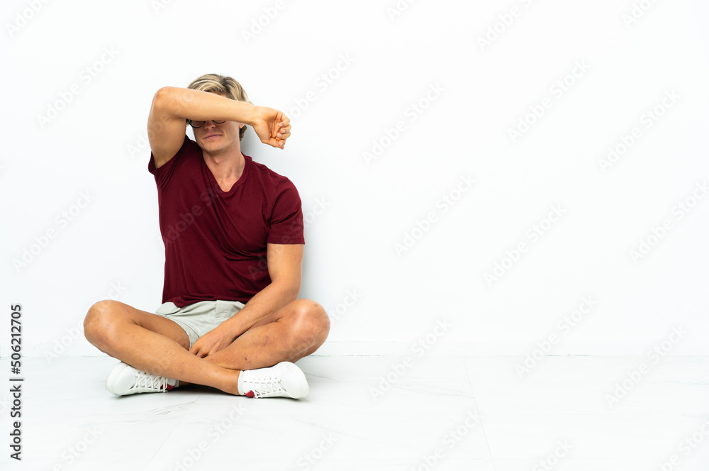 Fototapeta premium Young English man sitting on the floor covering eyes by hands