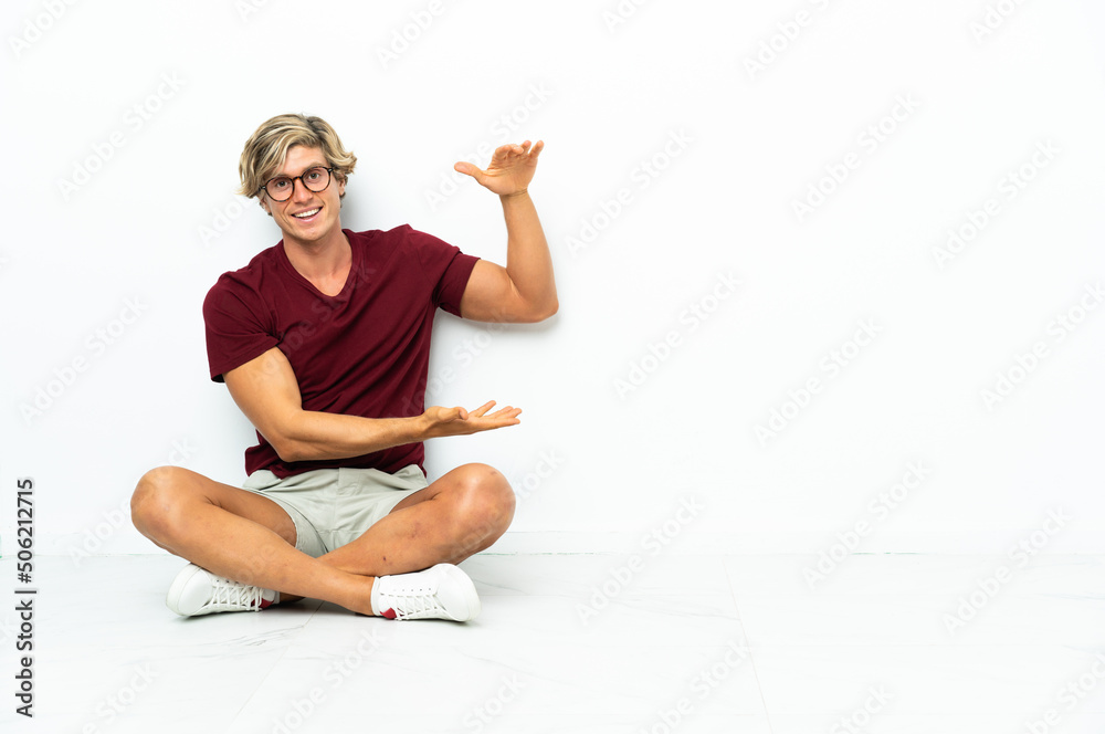 Young English man sitting on the floor holding copyspace to insert an ad