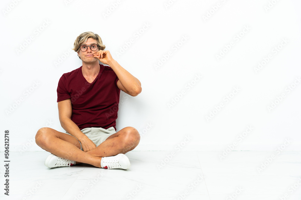 Young English man sitting on the floor showing a sign of silence gesture Young English man sitting on the floor showing a sign of silence gesture