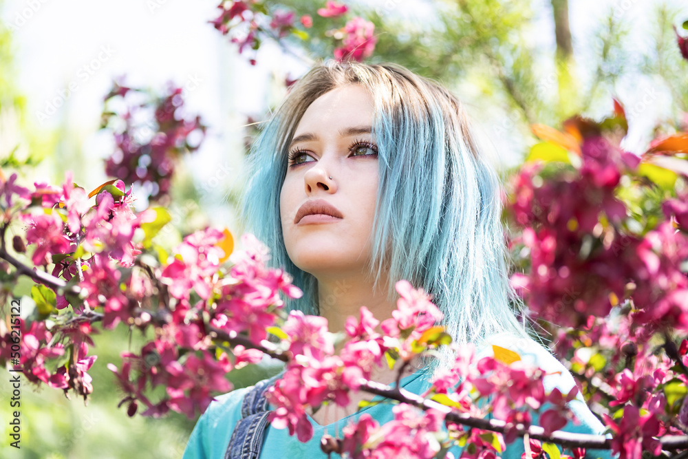 Portrait of blue haired woman against pink blossom trees at sunny day. Portrait of blue haired woman against pink blossom trees at sunny day.