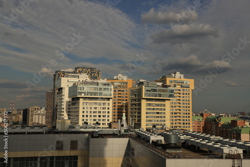 Panorama of the city with modern high-rise residential complexes, roofs of buildings and expressive clouds in the blue sky.