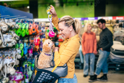 Beautiful middle aged blond woman buying accessories and food for her poodle puppy in pet shop. photo
