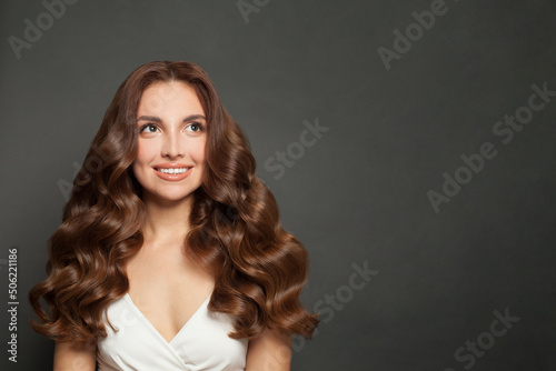 Pretty young woman with long wavy brown hair smiling and looking up on black background
