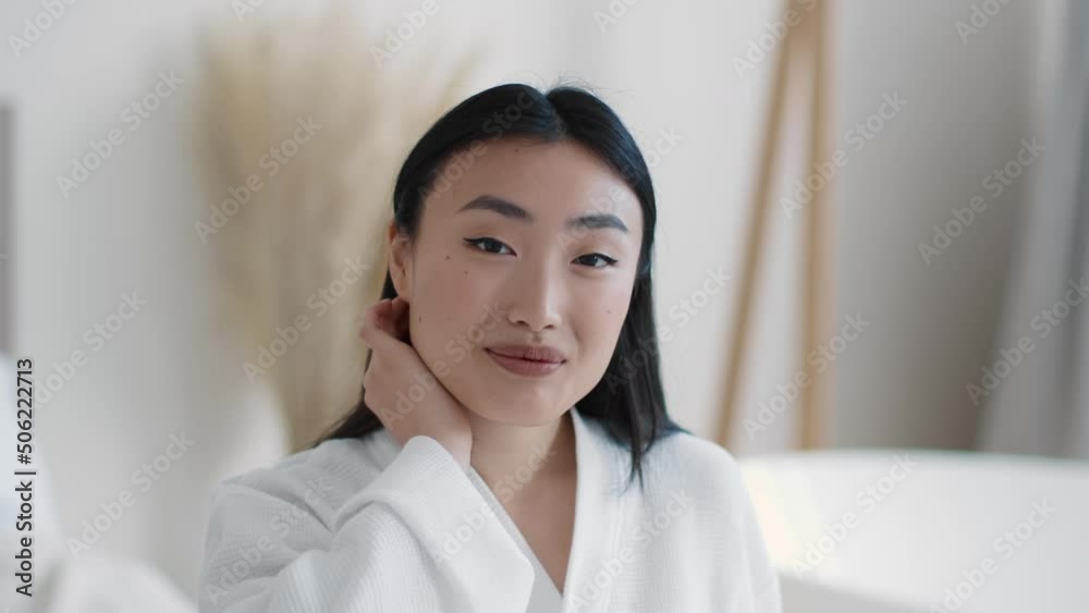 Beauty portrait of young well-groomed asian woman fixing hair and smiling to camera, sitting at bathroom, slow motion Beauty portrait of young well-groomed asian woman fixing hair and smiling to camera, sitting at bathroom, slow motion