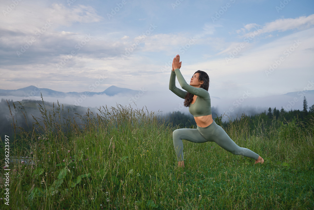 Young dark haired woman in sport outfit having yoga practice among green mountains. Concept of people, wellbeing and body care. Young dark haired woman in sport outfit having yoga practice among green mountains. Concept of people, wellbeing and body care.