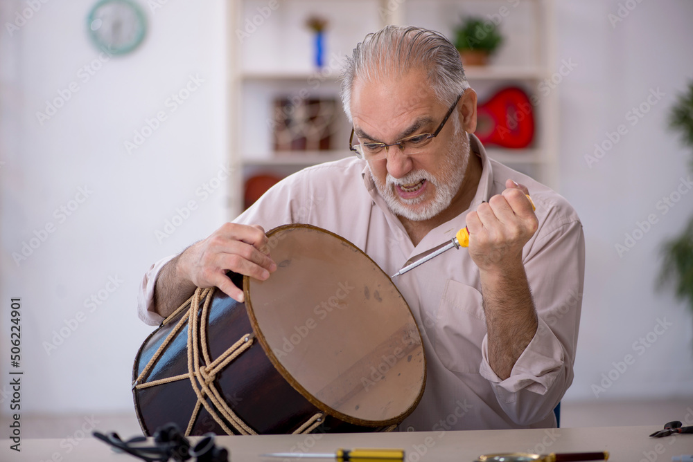 Fototapeta premium Old male repairman repairing musical instruments at workshop