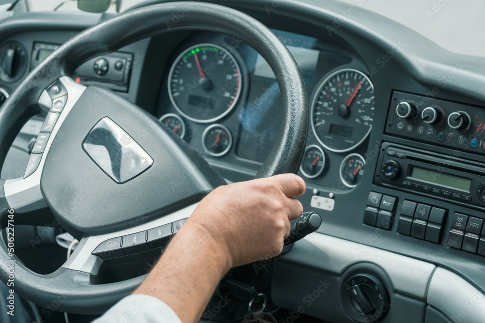Hand of a driver on steering wheel at intercity coach bus. Focus on steering wheel. Blurry control panel buttons and dials on the background. Man driving bus on the highway.