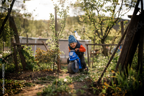 Little boy playing outdoors in country garden, child riding motorcycle. Funny childhood, lifestyle, family concept.