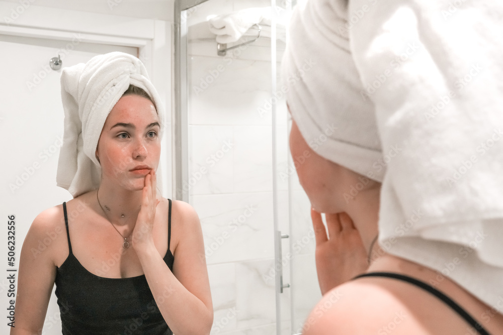 Fototapeta premium Beauty concept. Wellness, taking care yourself. Portrait beautiful woman looking in the mirror in the bathroom.Beautiful girl bath towel her head, taking care of herself, gouache massage, mask, spa