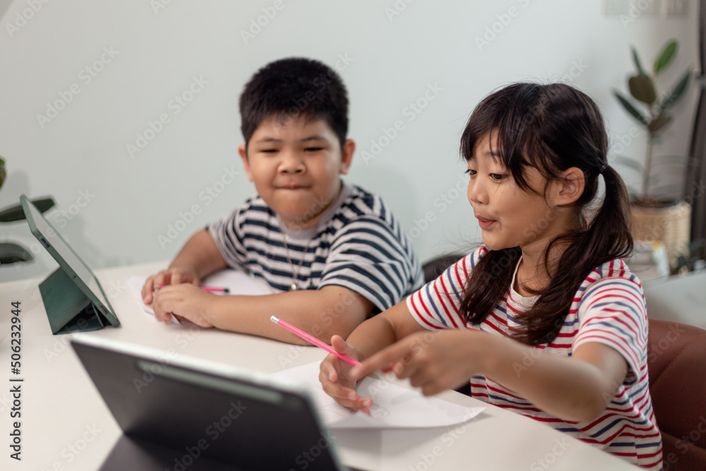Asian boys and girls enjoy online learning by taking notes and using tablets at home. Asian boys and girls enjoy online learning by taking notes and using tablets at home.