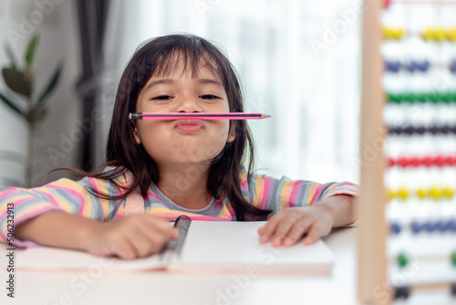 funny girl playing holding pen between nose and lips as mustache looking at the camera, playful bored after learning long hours. photo