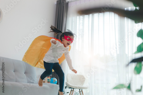 Girls child jumping on home living room couch wearing improvised superhero outfit fancy dress, playing having fun with energetic games, indoors. Discovery kids activities holiday lifestyle. photo