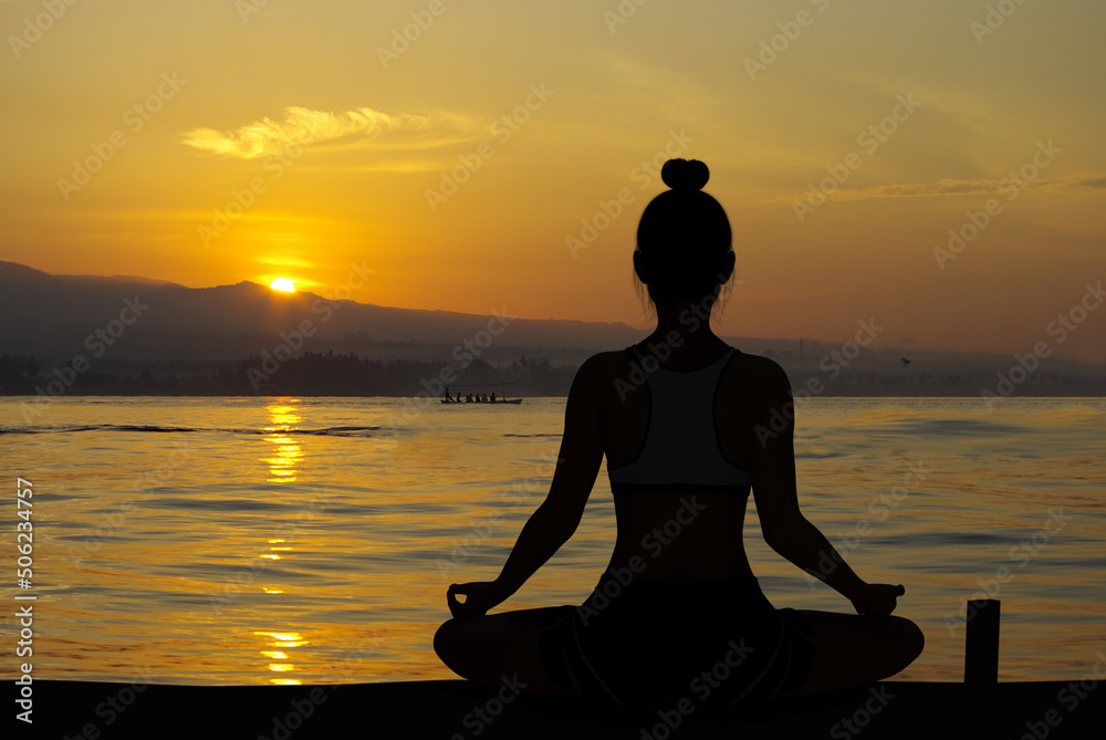 Woman silhouette in Yoga Easy Meditating pose at sunrise with very quiet ocean