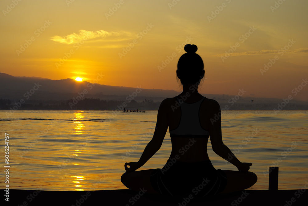 Woman silhouette in Yoga Easy Meditating pose at sunrise with very quiet ocean Woman silhouette in Yoga Easy Meditating pose at sunrise with very quiet ocean