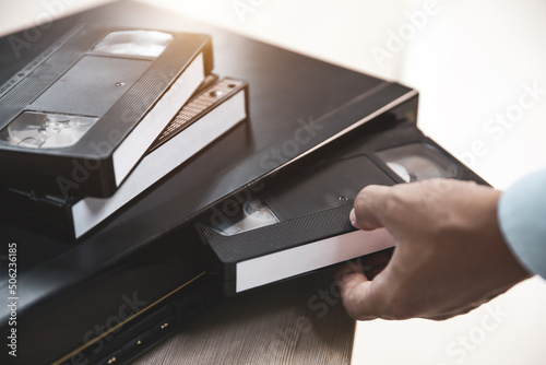 фотографія Close-up hand put or insert video cassette tape VHS old retro style on video record playback concept of vintage electric and electronic appliances multimedia player device old fashioned