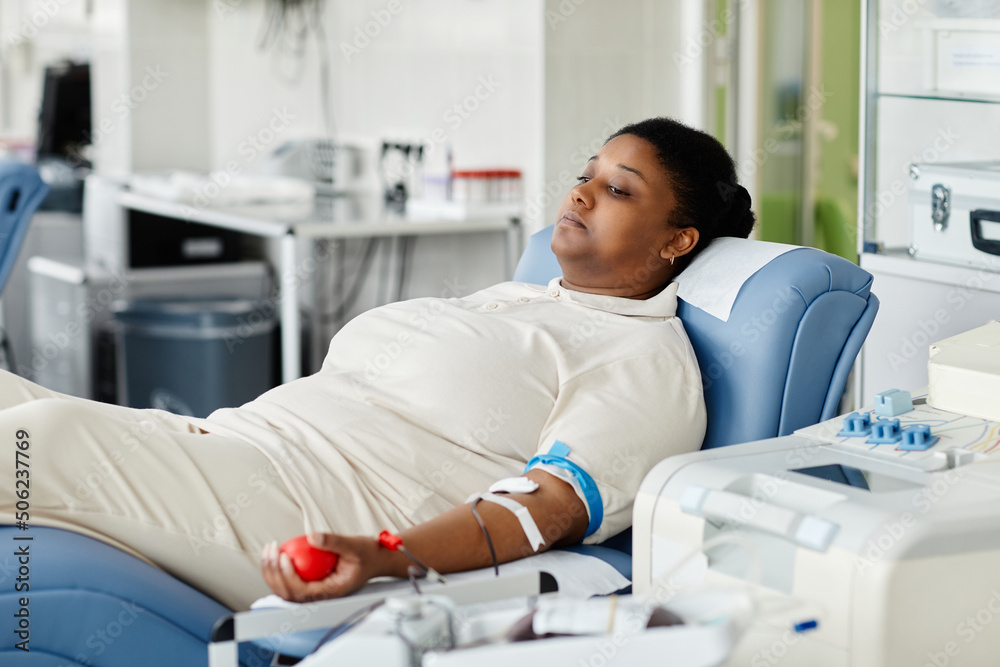 Fototapeta premium Portrait of young African American woman giving blood while laying in chair at plasma donation center