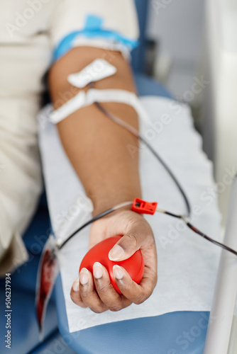 Close up of unrecognizable African American woman giving blood while laying in chair at blood donation center, female hand squeezing stress ball