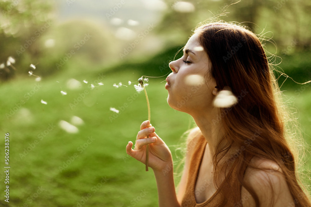 A female freelancer strolls carefree and happily in a green park and blows off a dandelion flower in the sunset light A female freelancer strolls carefree and happily in a green park and blows off a dandelion flower in the sunset light