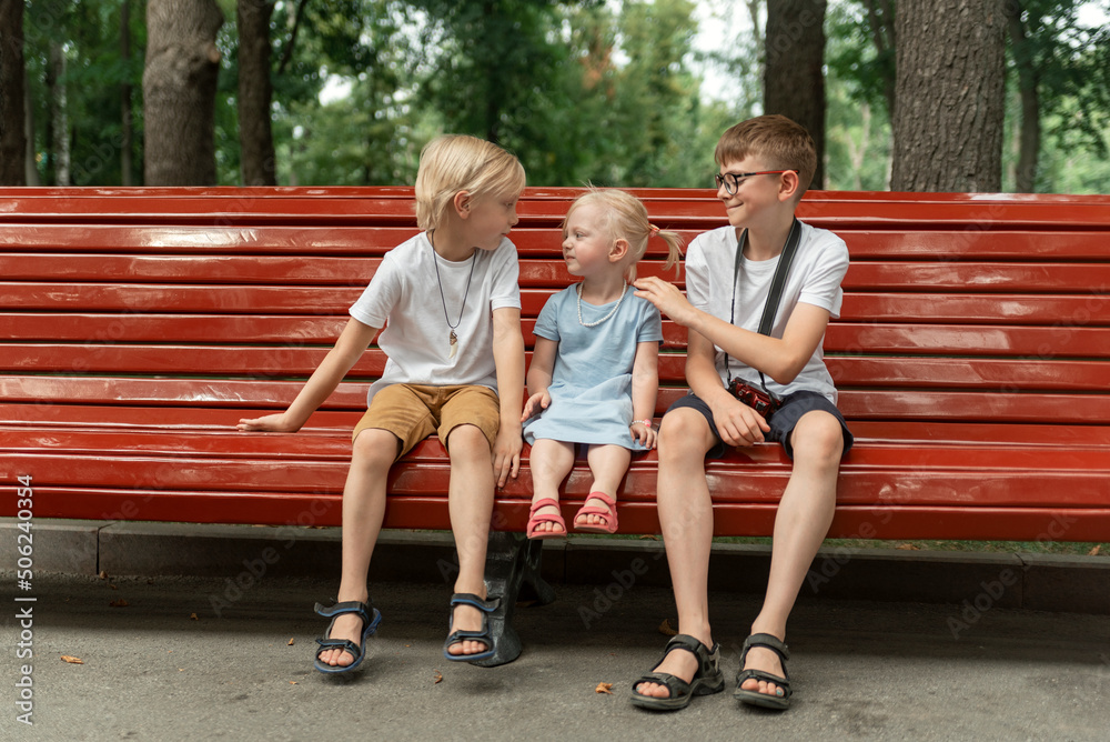 Little sister and two older brothers are resting in park on summer day. Portrait of siblings sit on bench. Little sister and two older brothers are resting in park on summer day. Portrait of siblings sit on bench.