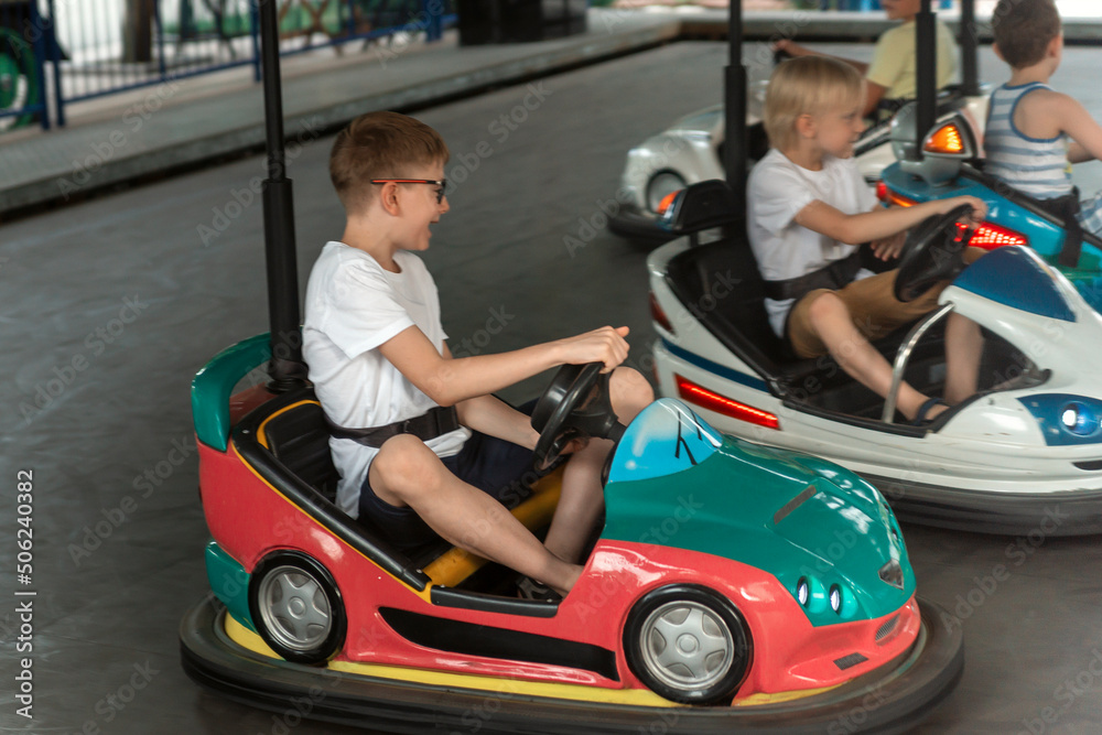 Boys driving bumper cars in an amusement park. Young drivers competing on mini car racing. Boys driving bumper cars in an amusement park. Young drivers competing on mini car racing.