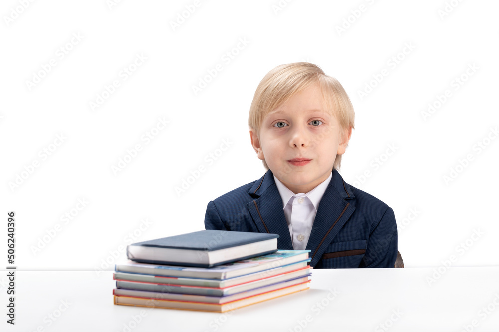 Portrait of cute blond boy in school uniform at table next to notebooks and textbook. Schoolboy and stationery. Portrait of cute blond boy in school uniform at table next to notebooks and textbook. Schoolboy and stationery.