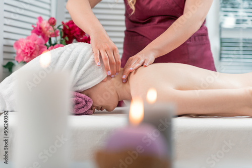 Woman enjoying relaxing back massage in cosmetology spa centre. Masseur makes neck massage.