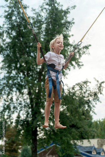 Portrait of boy jumping on trampoline in an amusement park. Child frolics and jumps high. Vertical frame.