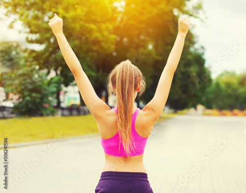 Fitness happy strong woman enjoying after training outdoors  runner winner  female model raising hands up in the park  rear view