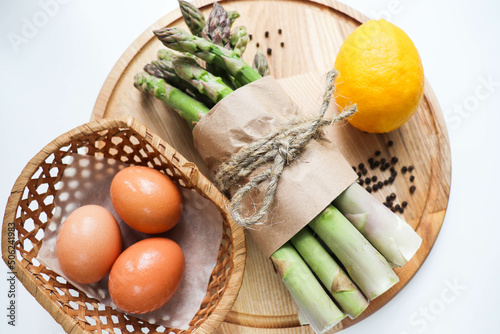 a bunch of asparagus  lemon  eggs and spices on a wooden table