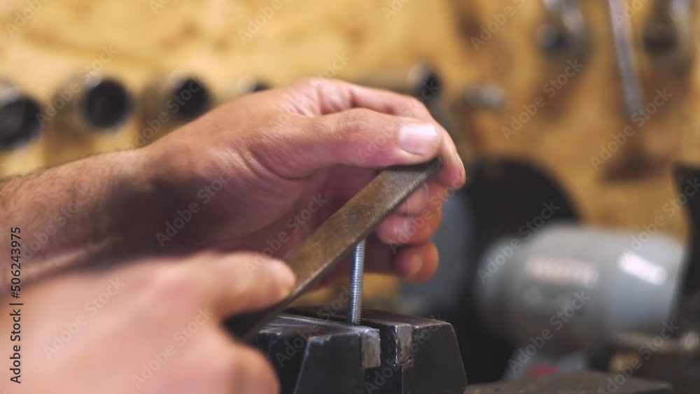 Male hands hold a grinding file. Detail processing. Work in the workshop. Private master. The light bolt is clamped in a vise. Close-up. Male hands hold a grinding file. Detail processing. Work in the workshop. Private master. The light bolt is clamped in a vise. Close-up.