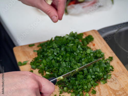 Part of a hand chopping green onions on a cutting board.