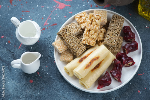 Plate with georgian traditional desserts including stuffed crepes, churchkhela and kozinaki, horizontal shot on a blue stone background photo